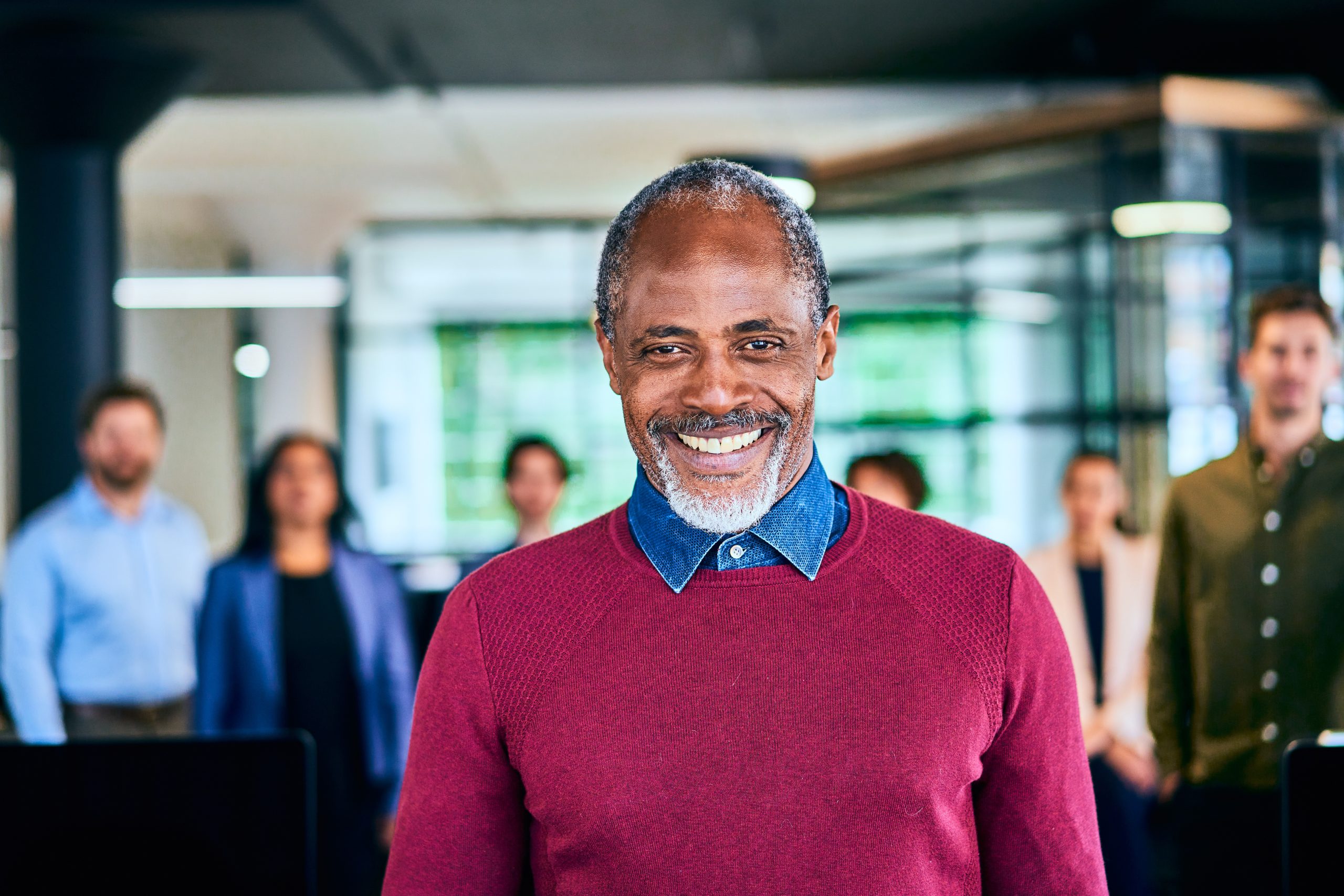 Portrait of a mature Black male manager smiling with his diverse team of designers standing in the background