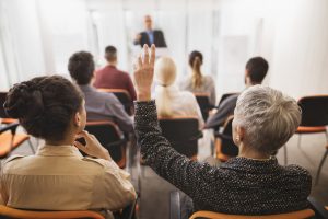 Rear view of a businesswoman raising her hand on education event. She wants to ask something.